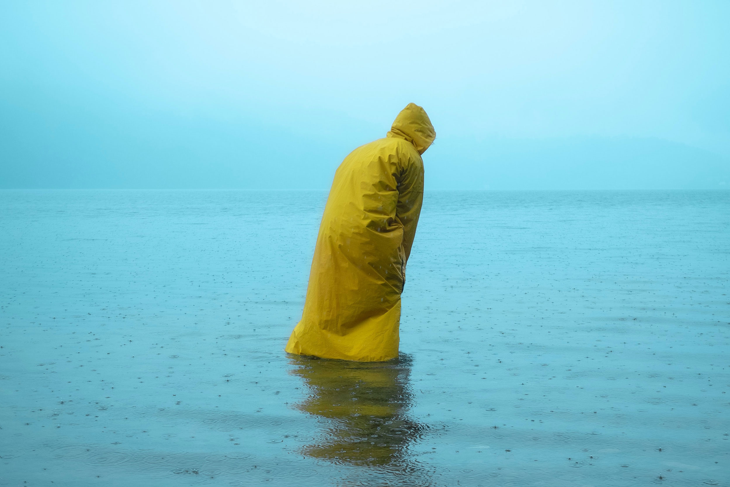 Figure in yellow raincoat wading in water.