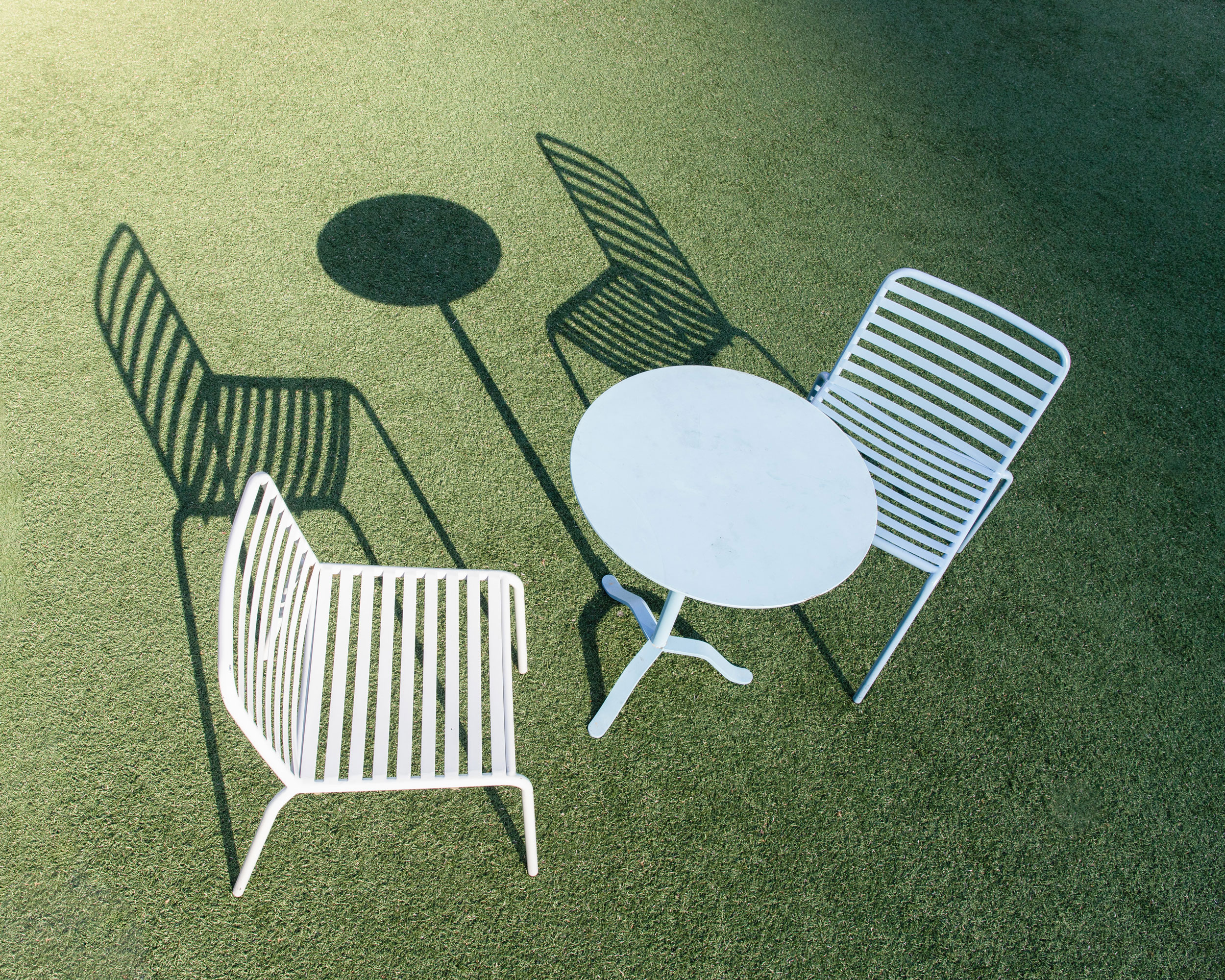 Two chairs and a table cast a shadow on green grass